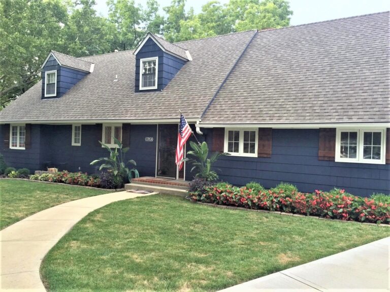 Blue Colonial-Style House With a Neatly Landscaped Front Yard and an American Flag Displayed Near the Entrance.